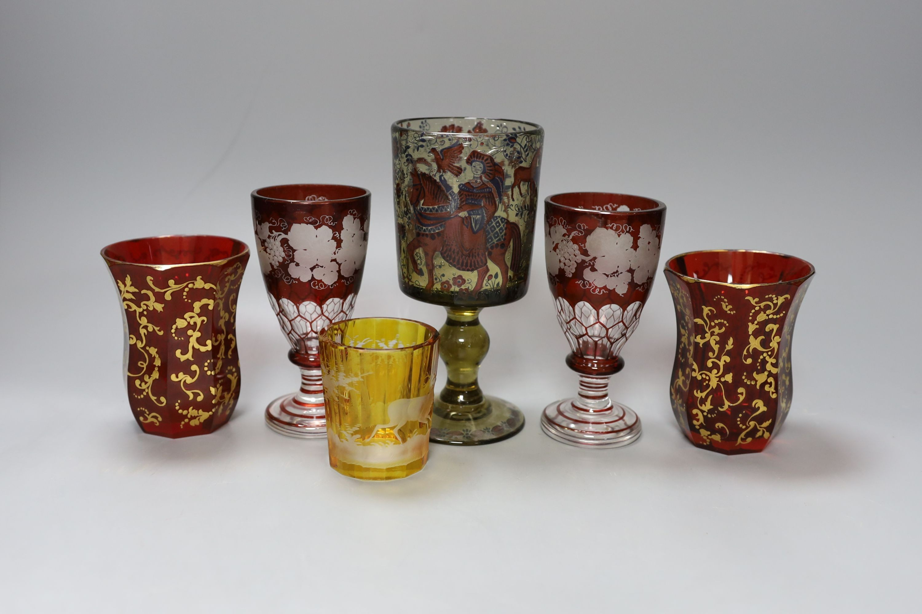 A group of Bohemian coloured glass, including a pair of vine-engraved ruby-flashed wine glasses, pair of gilded ruby glass beakers, a stag engraved, amber-flashed beaker and a Historismus goblet, 17cm